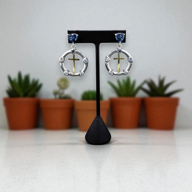 Pair of earrings on a black stand with potted plants in the background